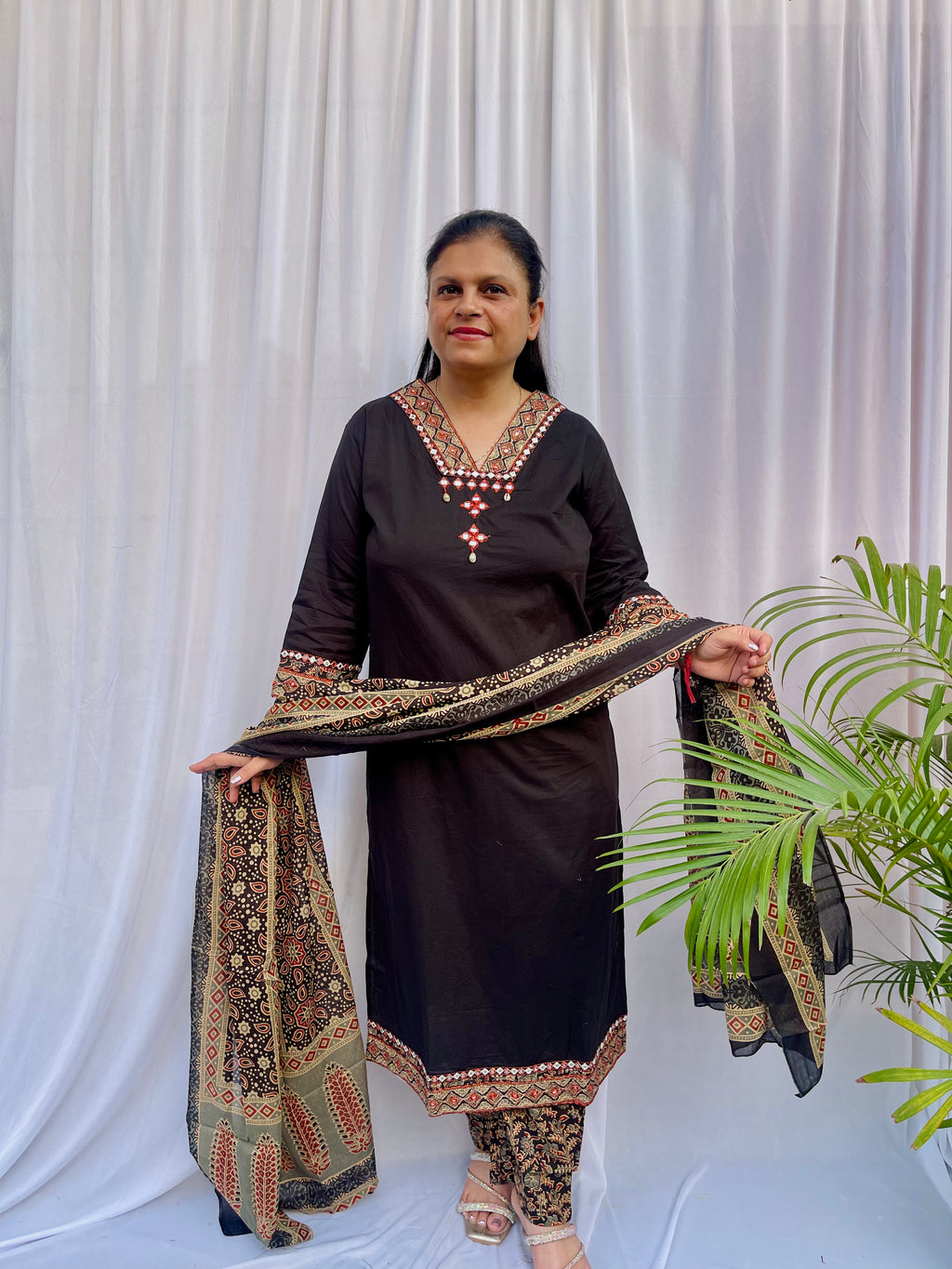 Woman wearing a black ethnic printed kurta set with matching pants and dupatta, featuring traditional motifs and a V-neck design.