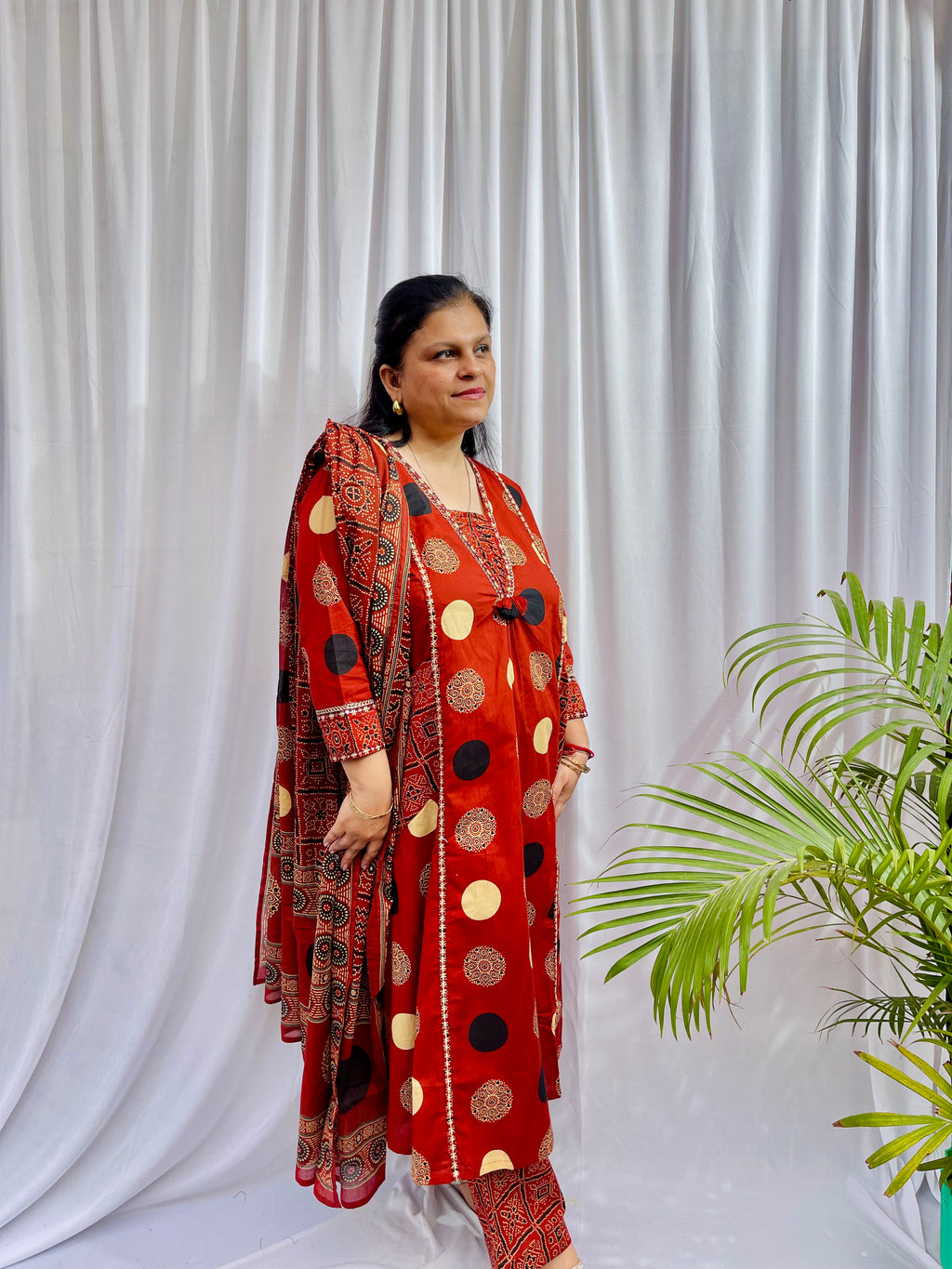 Woman wearing a rust red printed kurta set with polka dot and geometric patterns, styled with a traditional Ajrakh-inspired dupatta.