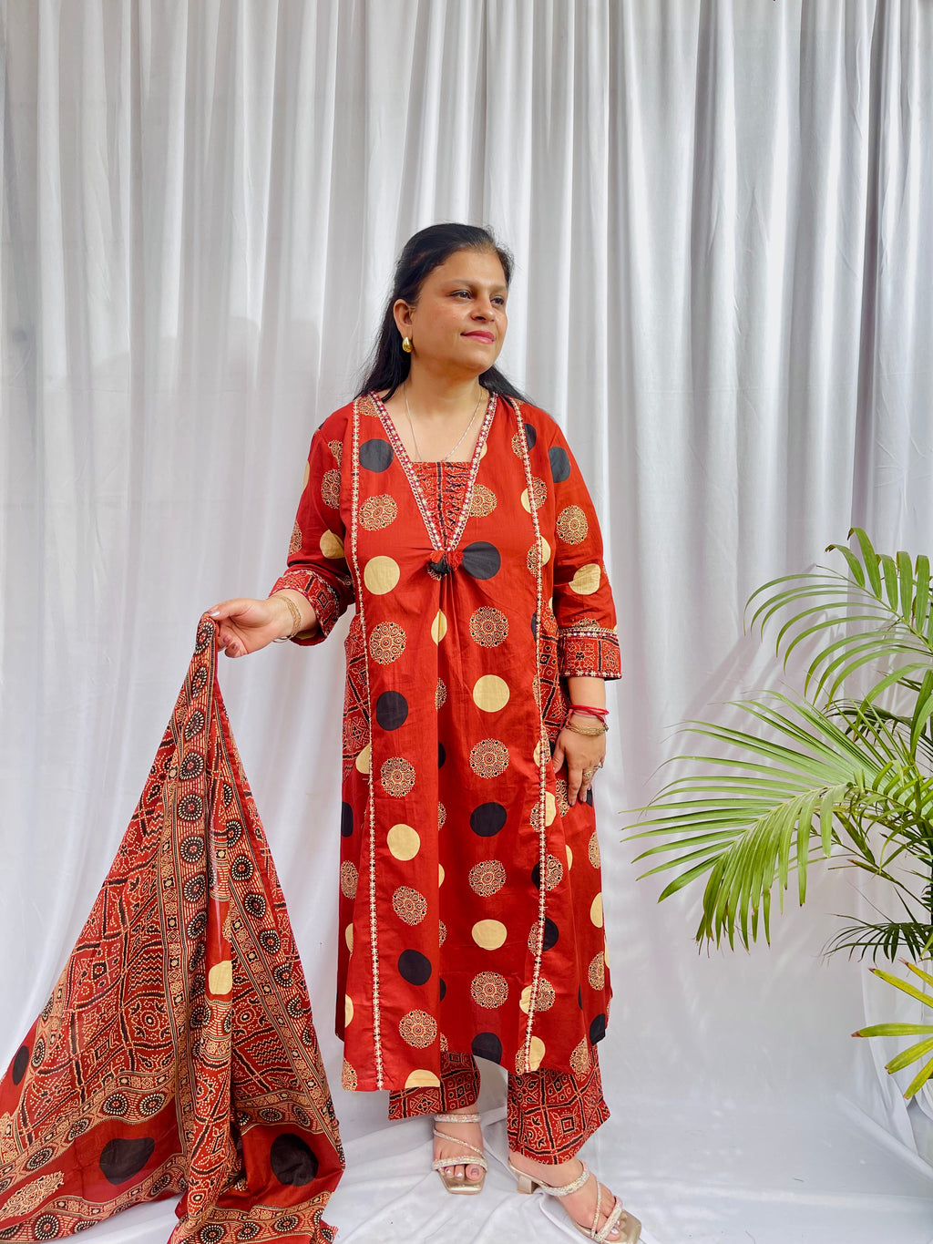 Woman wearing a rust red printed kurta set with polka dot and geometric patterns, styled with a traditional Ajrakh-inspired dupatta.