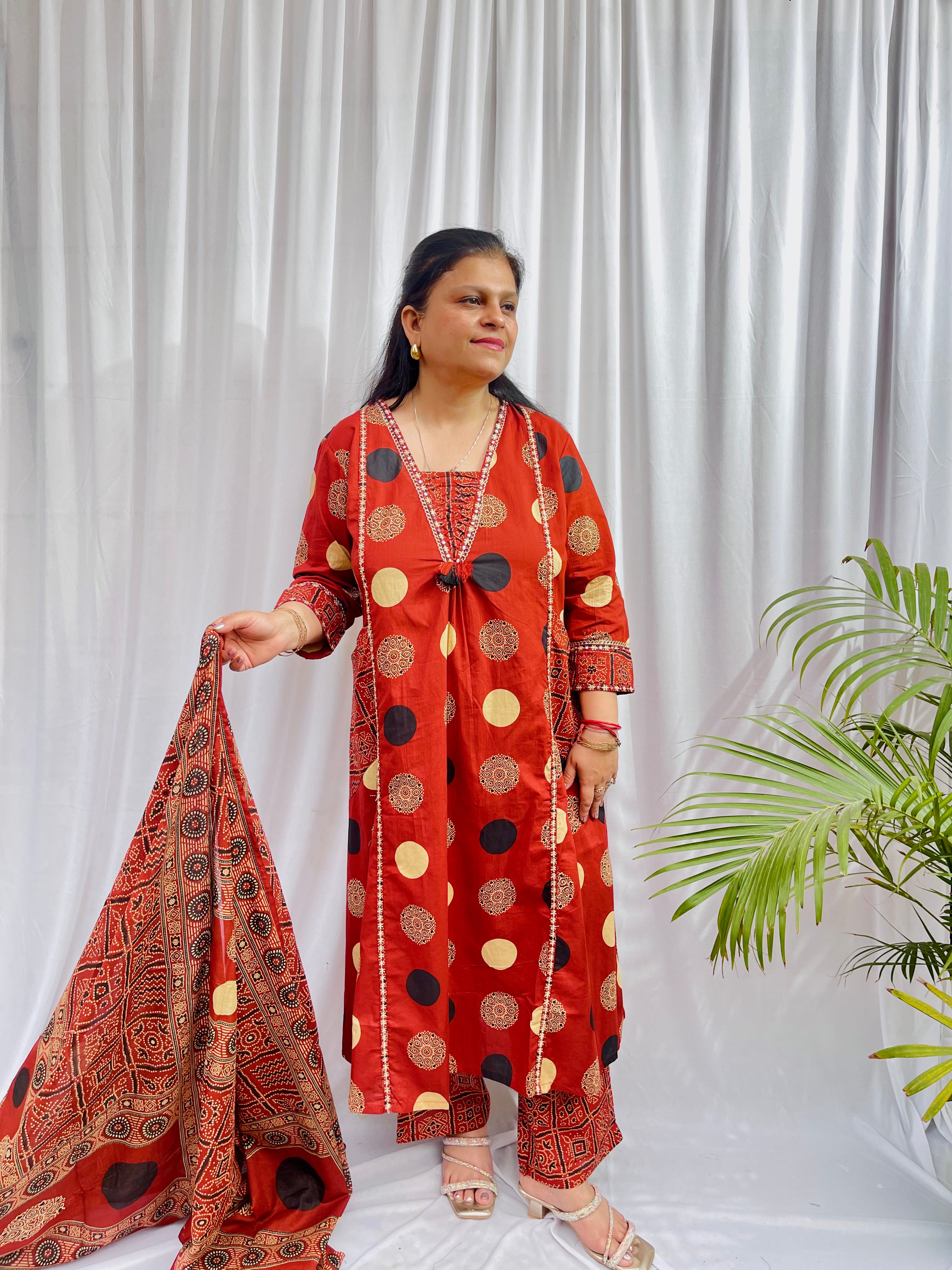 Woman wearing a rust red printed kurta set with polka dot and geometric patterns, styled with a traditional Ajrakh-inspired dupatta.