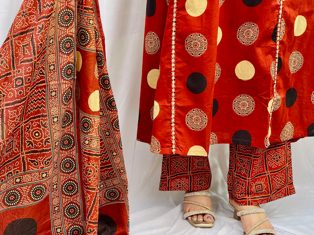 Woman wearing a rust red printed kurta set with polka dot and geometric patterns, styled with a traditional Ajrakh-inspired dupatta.