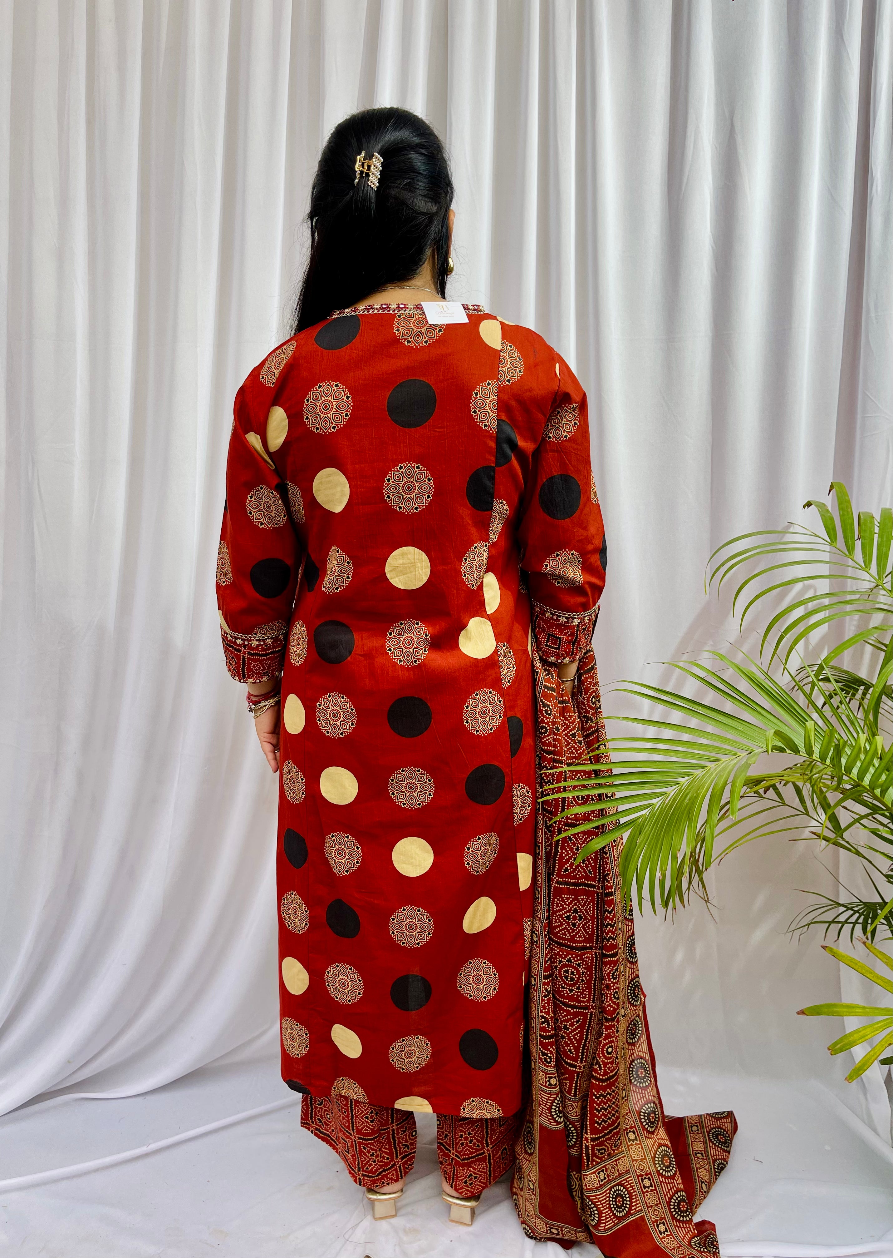 Woman wearing a rust red printed kurta set with polka dot and geometric patterns, styled with a traditional Ajrakh-inspired dupatta.