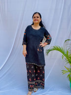 Model posing in a midnight black tunic with floral embroidered sleeves and wide-leg trousers featuring traditional elephant motifs.