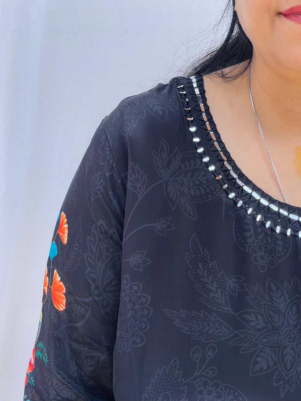 Model posing in a midnight black tunic with floral embroidered sleeves and wide-leg trousers featuring traditional elephant motifs.