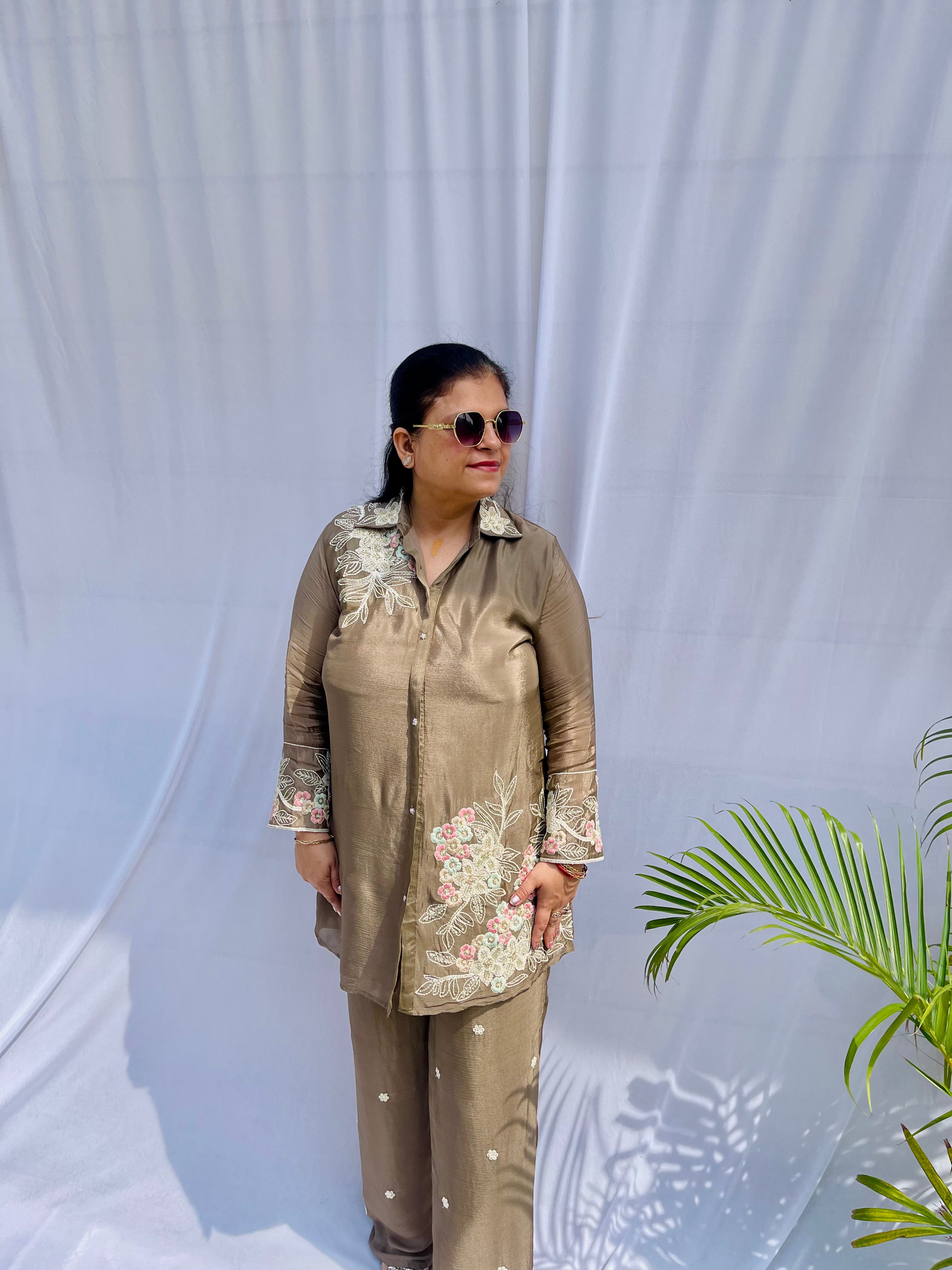 Woman in a metallic bronze silk shirt set with delicate pastel floral threadwork on the collar, hem, and cuffs.