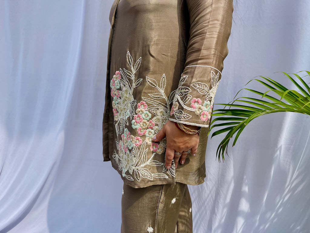Woman in a metallic bronze silk shirt set with delicate pastel floral threadwork on the collar, hem, and cuffs.