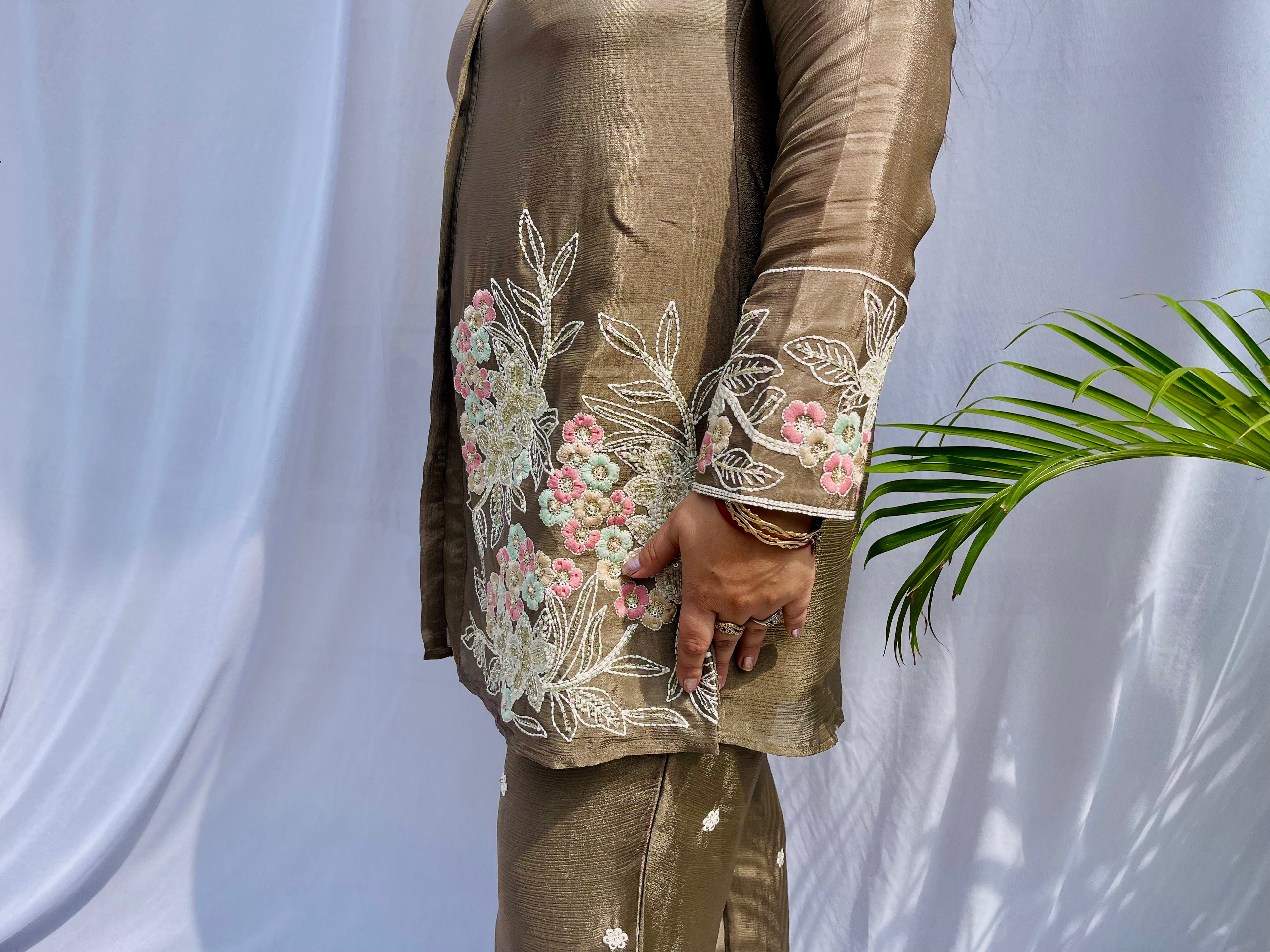 Woman in a metallic bronze silk shirt set with delicate pastel floral threadwork on the collar, hem, and cuffs.
