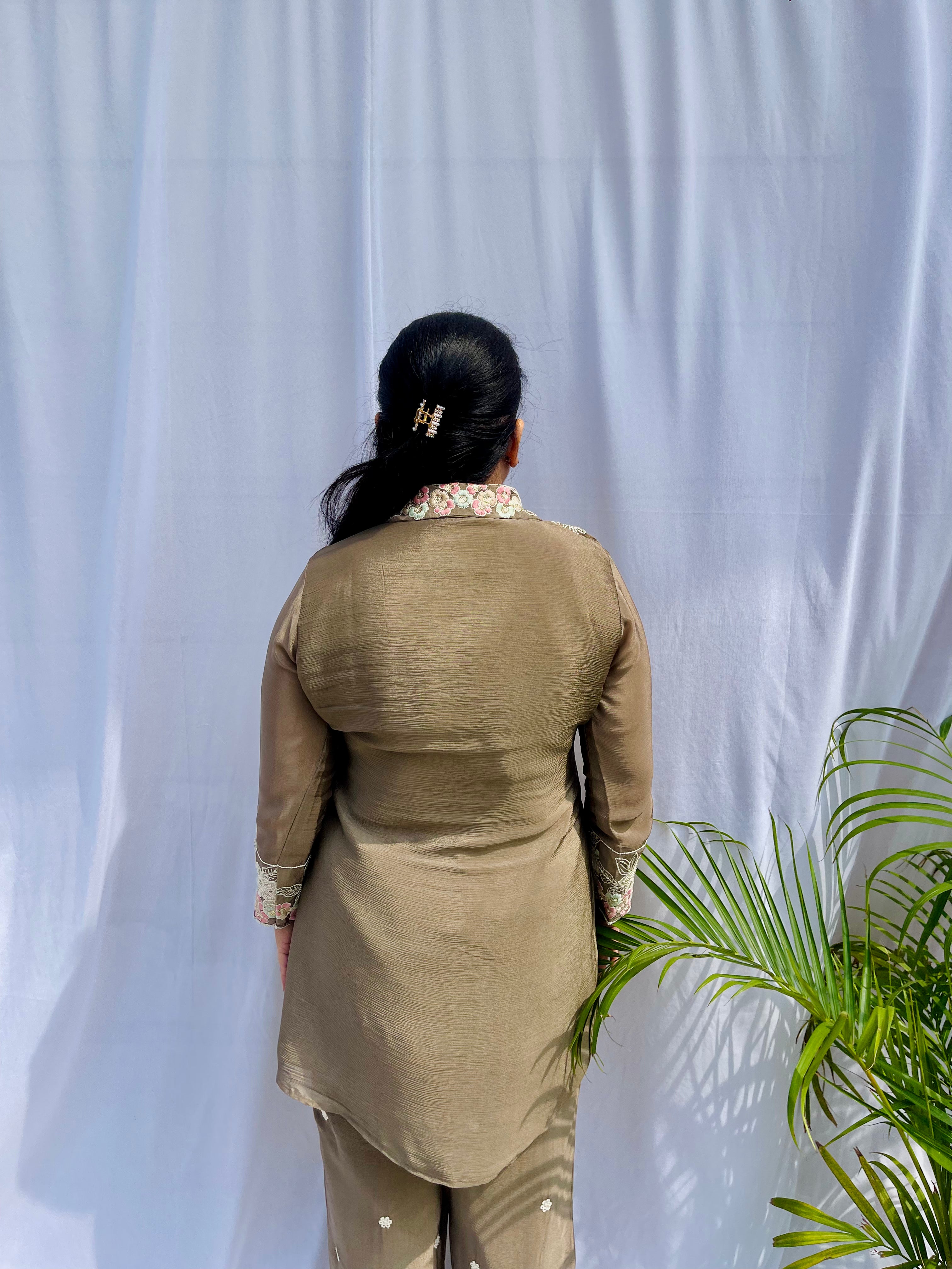 Woman in a metallic bronze silk shirt set with delicate pastel floral threadwork on the collar, hem, and cuffs.