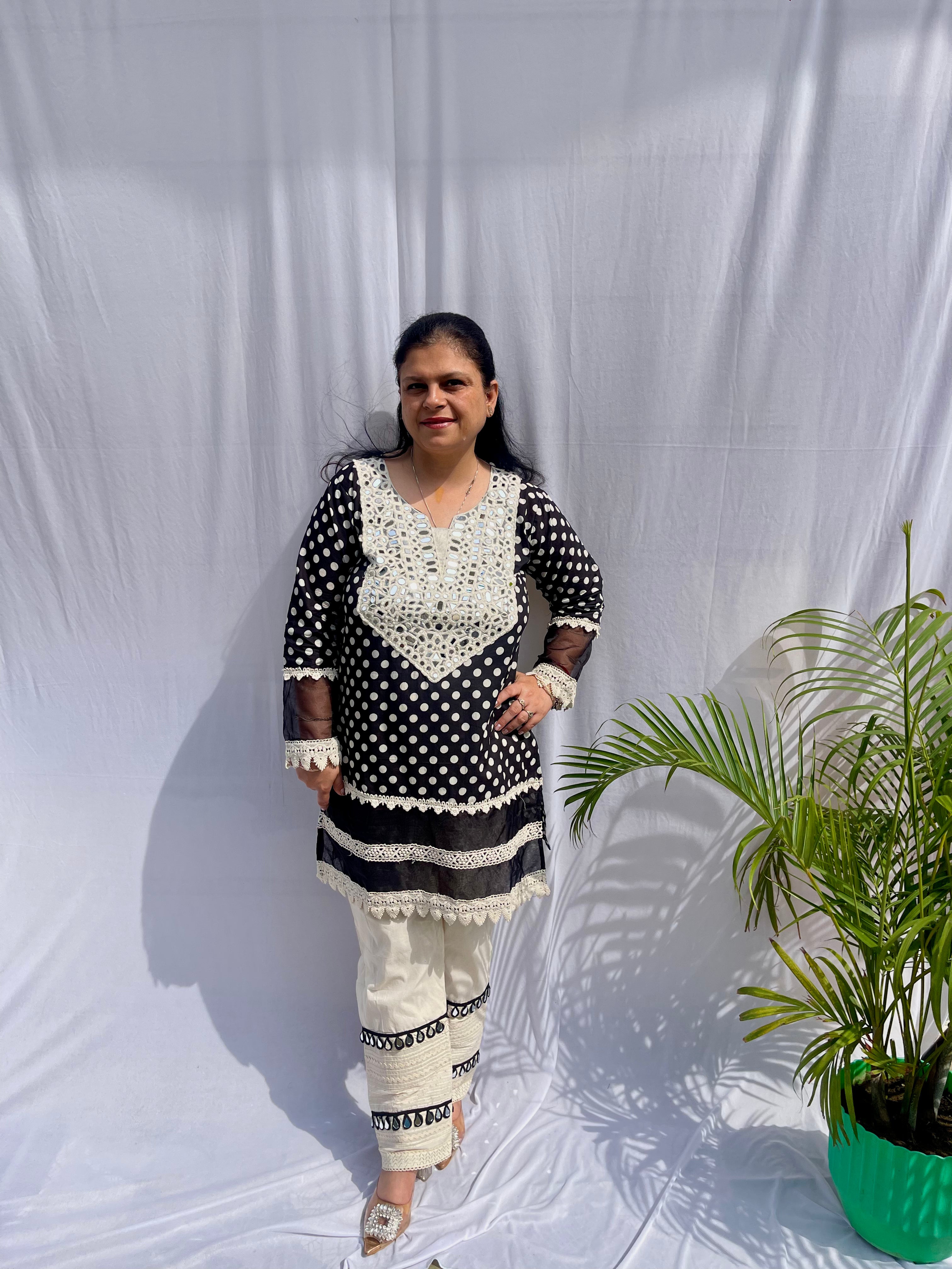 Black and white polka dot tunic featuring a V-shaped mirror work yoke, lace inserts, and matching white pants with mirror detailing.