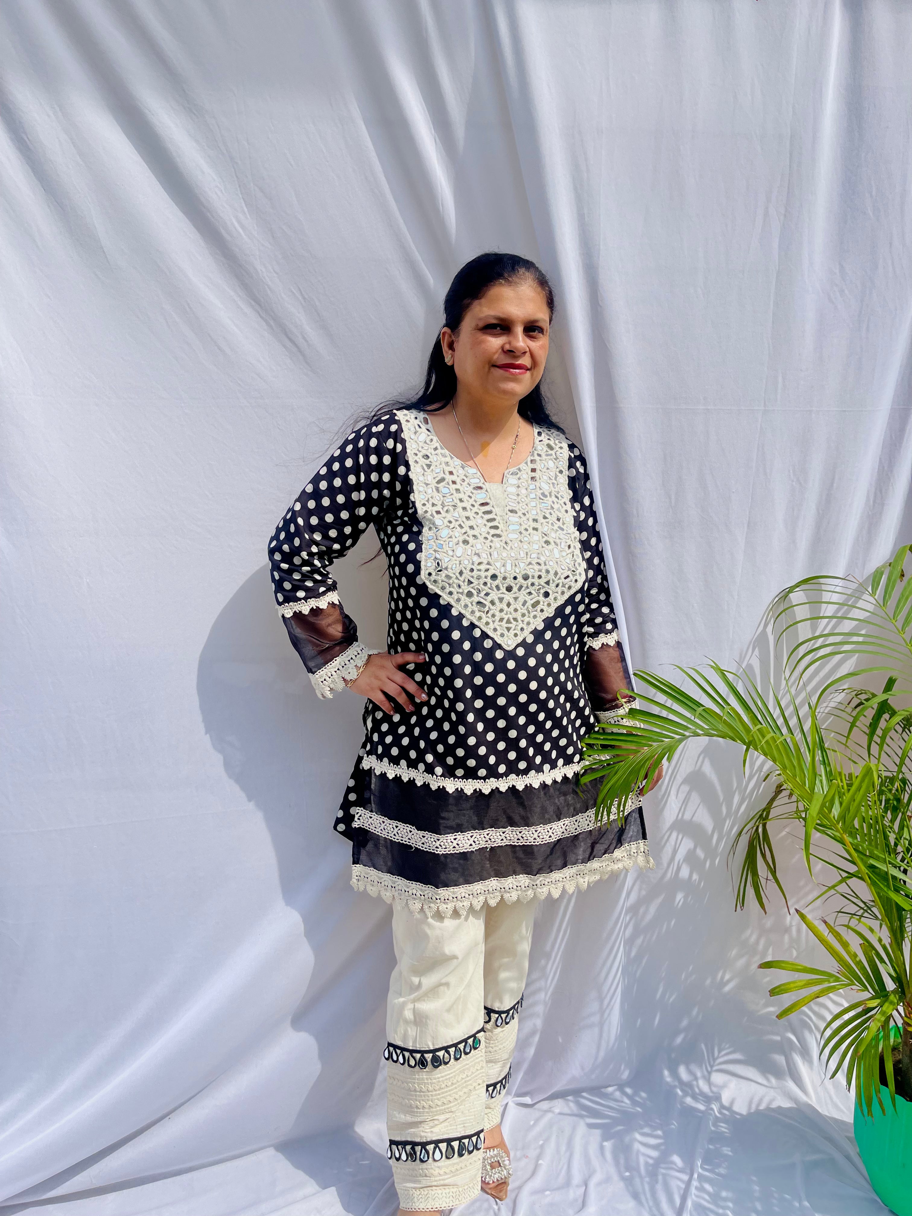 Black and white polka dot tunic featuring a V-shaped mirror work yoke, lace inserts, and matching white pants with mirror detailing.