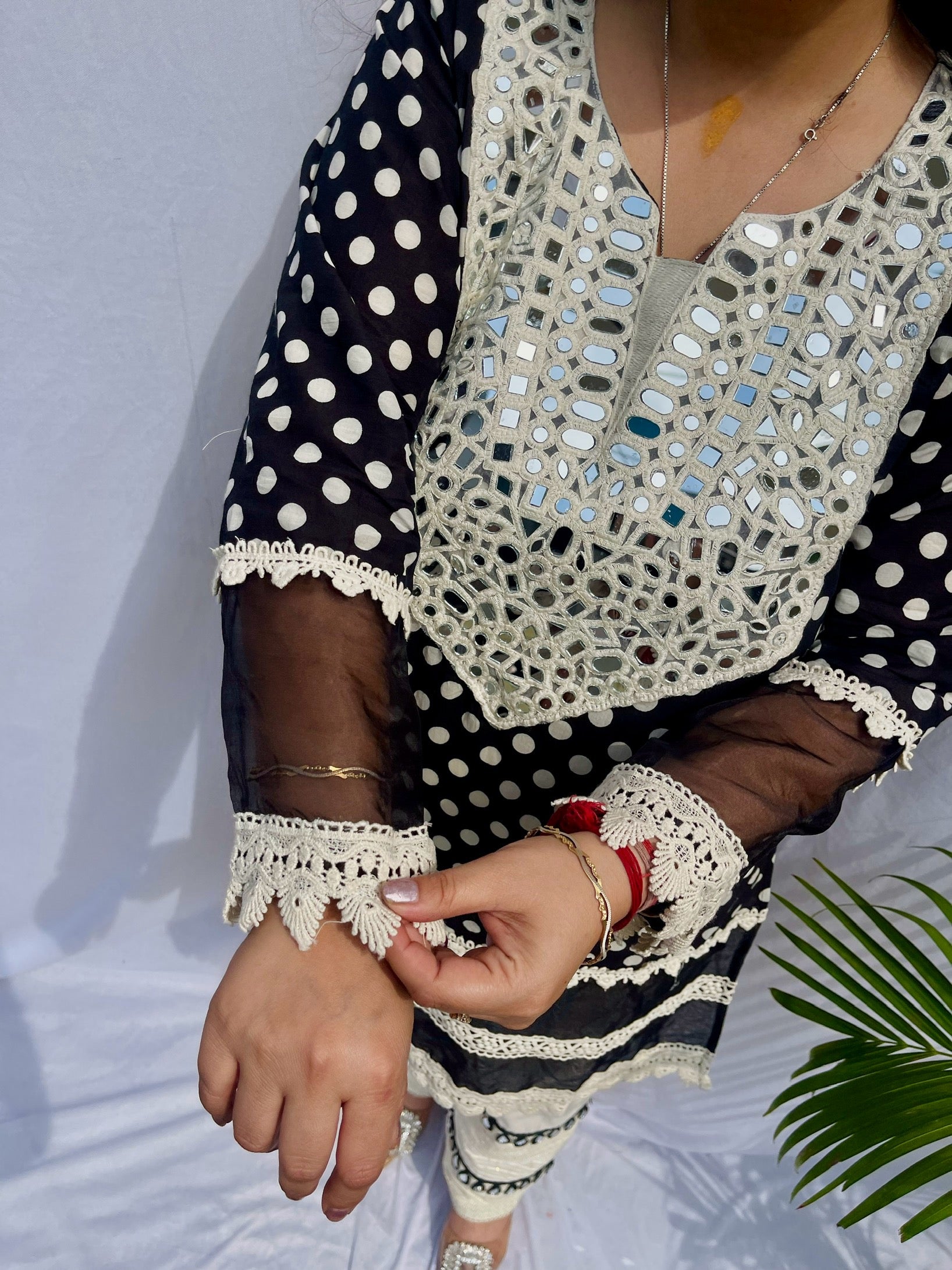 Black and white polka dot tunic featuring a V-shaped mirror work yoke, lace inserts, and matching white pants with mirror detailing.