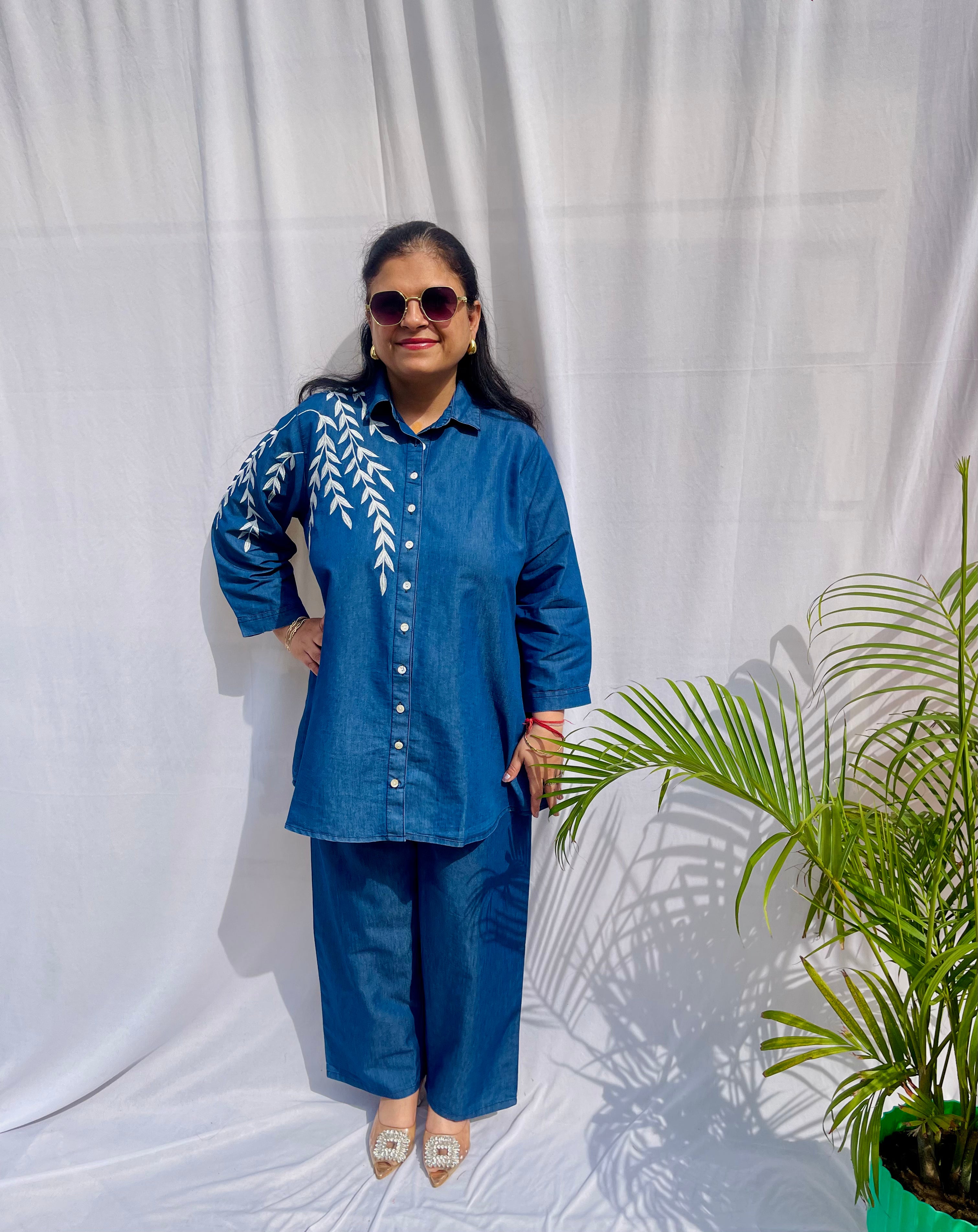 Denim-finish indigo blue shirt set with a large white leaf thread-work embroidery on the right shoulder and sleeve.