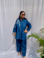 Denim-finish indigo blue shirt set with a large white leaf thread-work embroidery on the right shoulder and sleeve.