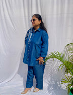 Denim-finish indigo blue shirt set with a large white leaf thread-work embroidery on the right shoulder and sleeve.