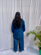 Denim-finish indigo blue shirt set with a large white leaf thread-work embroidery on the right shoulder and sleeve.
