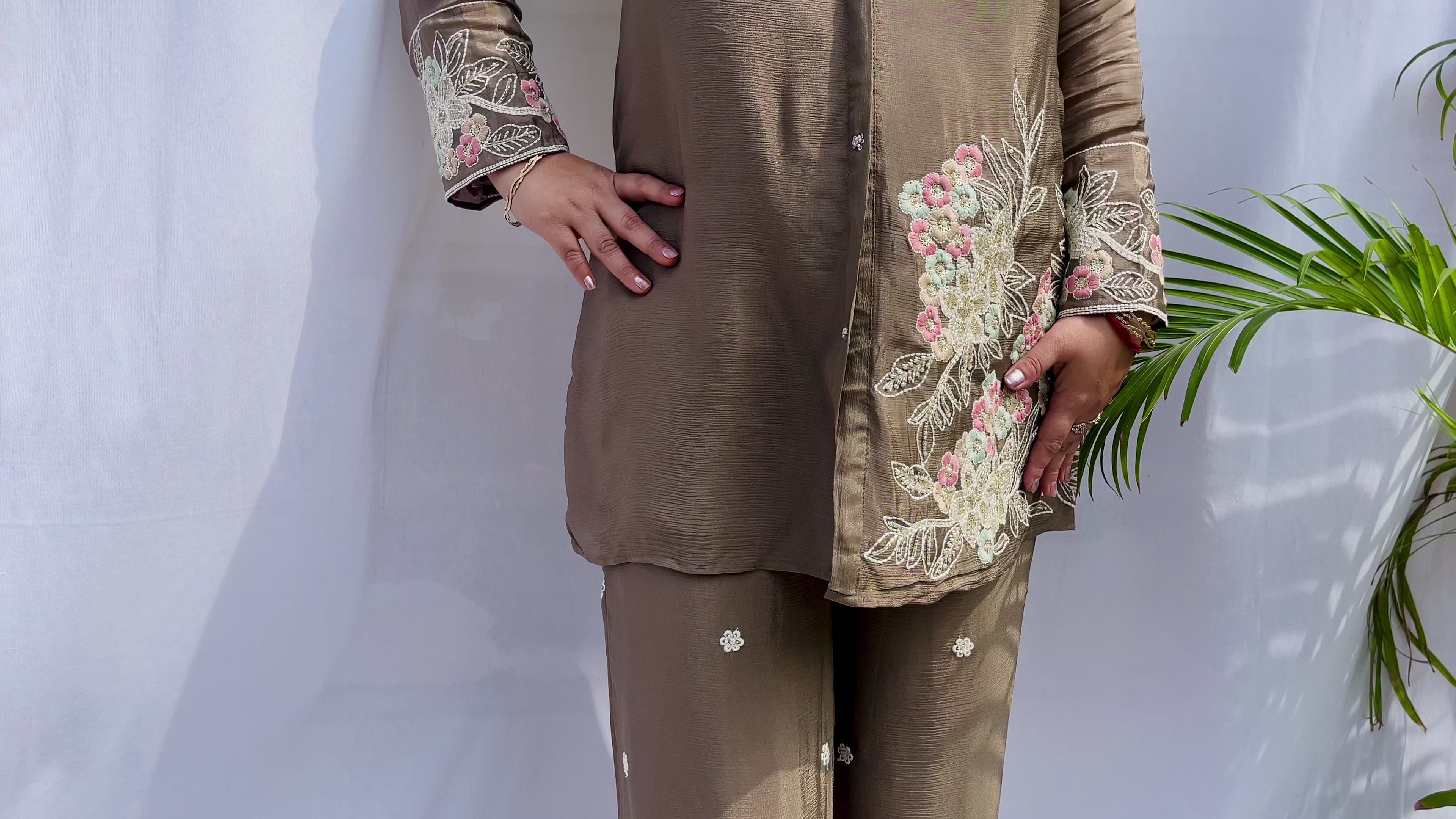 Woman in a metallic bronze silk shirt set with delicate pastel floral threadwork on the collar, hem, and cuffs.