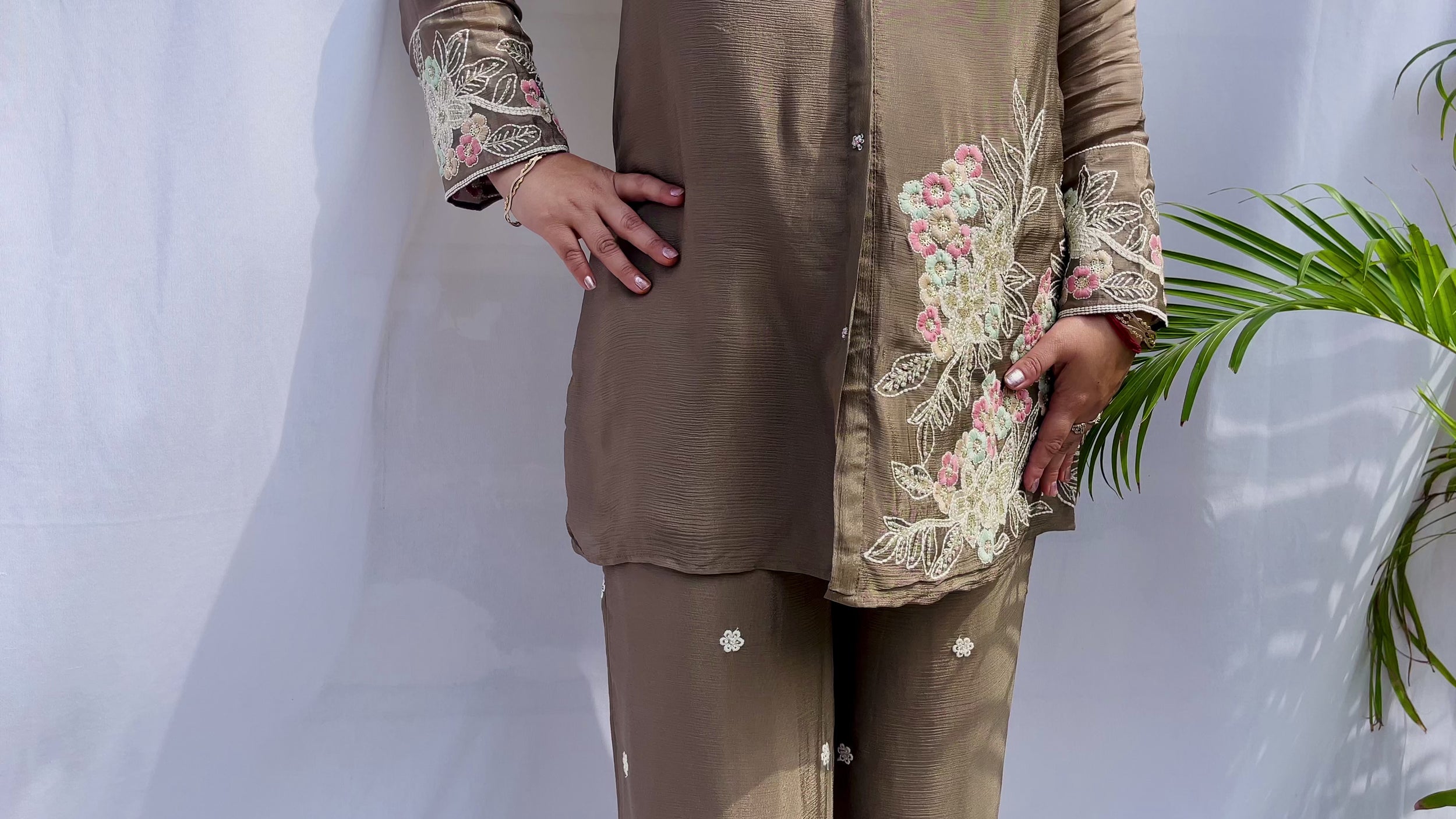 Woman in a metallic bronze silk shirt set with delicate pastel floral threadwork on the collar, hem, and cuffs.