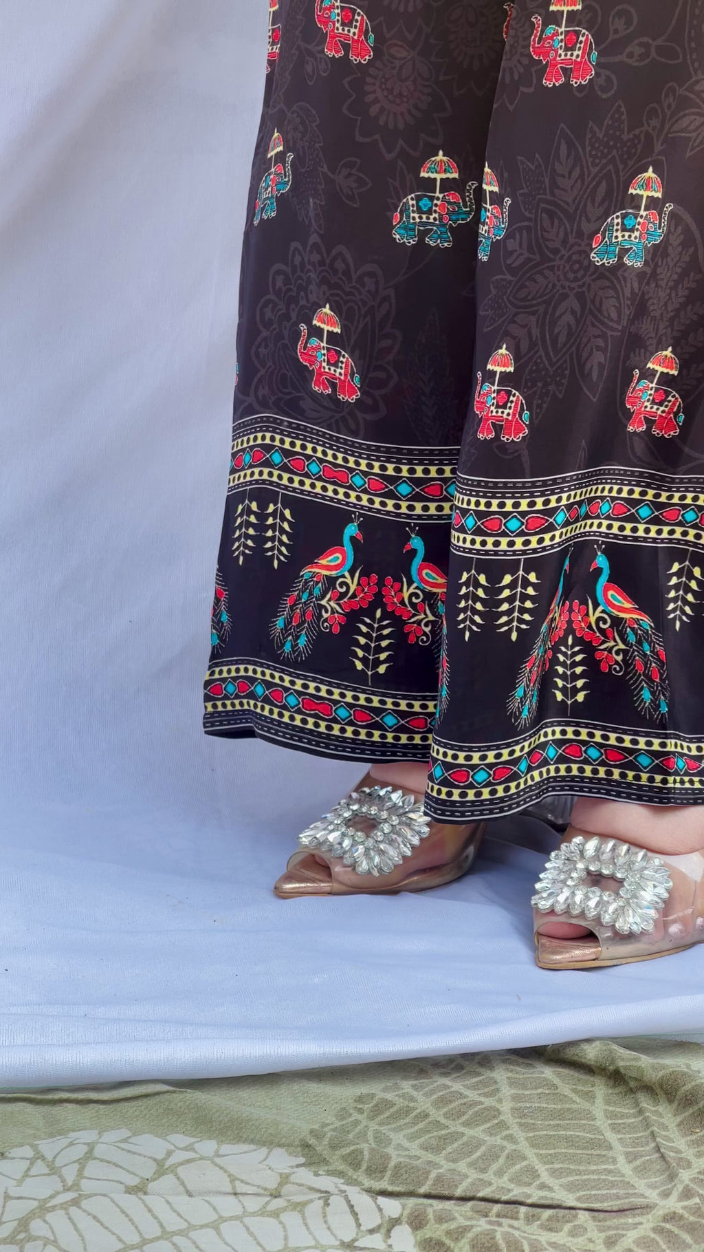 Model posing in a midnight black tunic with floral embroidered sleeves and wide-leg trousers featuring traditional elephant motifs.