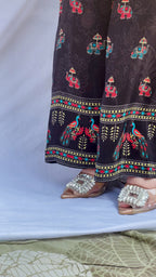 Model posing in a midnight black tunic with floral embroidered sleeves and wide-leg trousers featuring traditional elephant motifs.