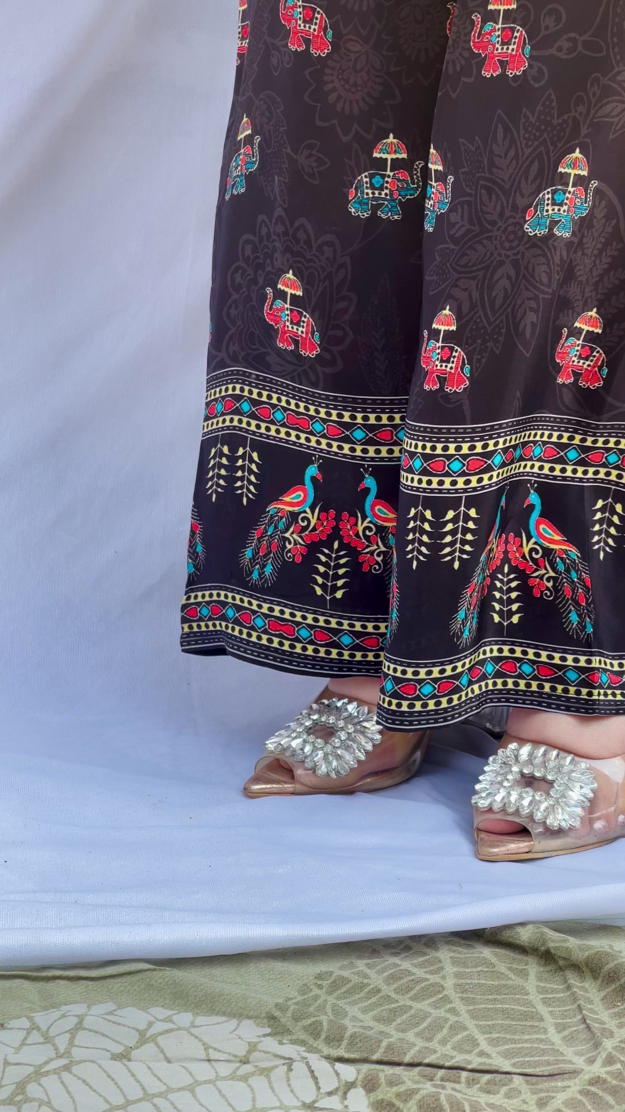 Model posing in a midnight black tunic with floral embroidered sleeves and wide-leg trousers featuring traditional elephant motifs.