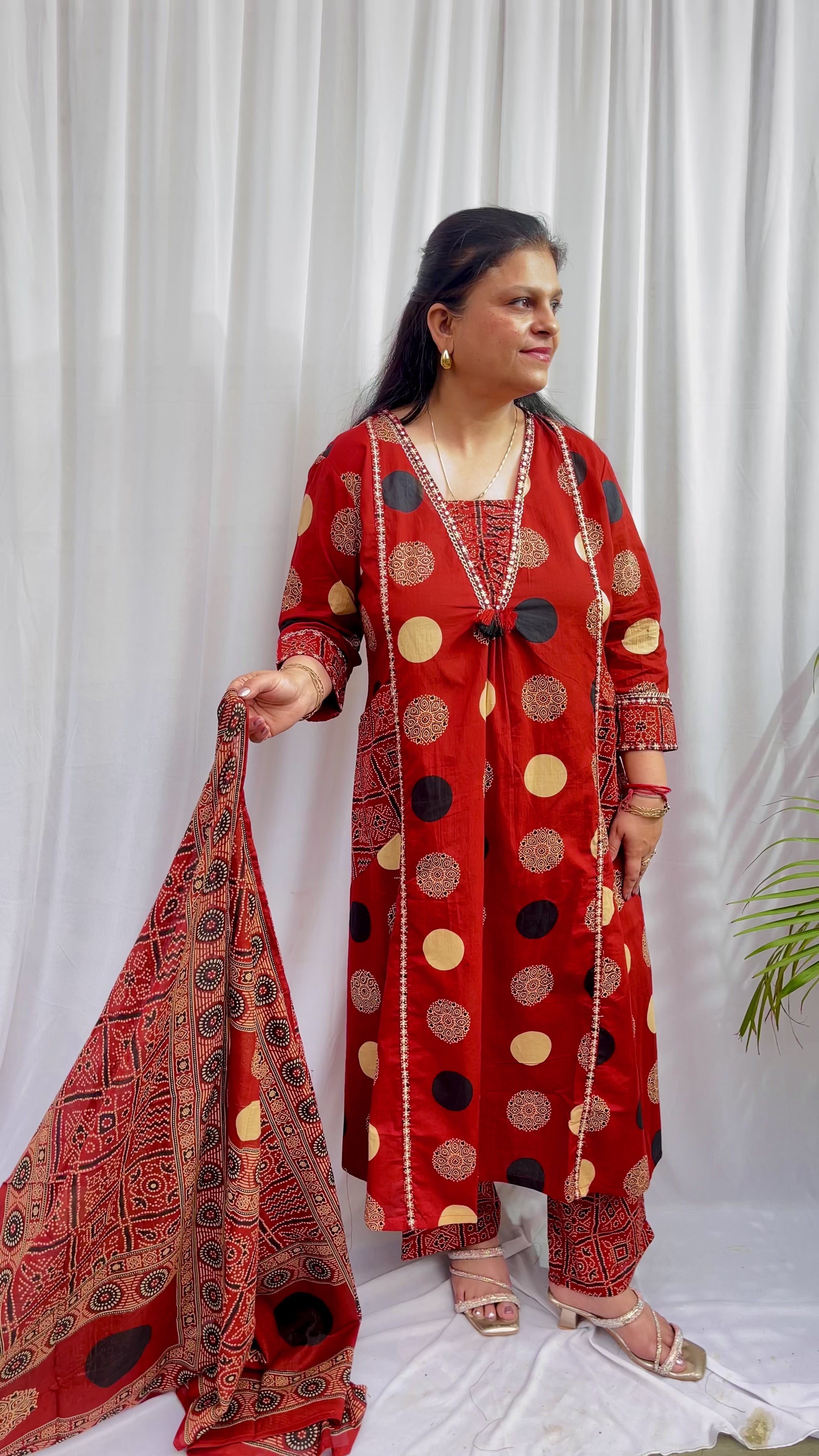 Woman wearing a rust red printed kurta set with polka dot and geometric patterns, styled with a traditional Ajrakh-inspired dupatta.